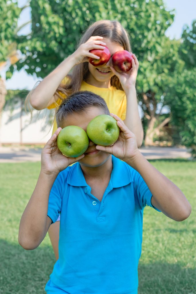 Cheerful teenagers children play with apples outdoors. Vertical shot.